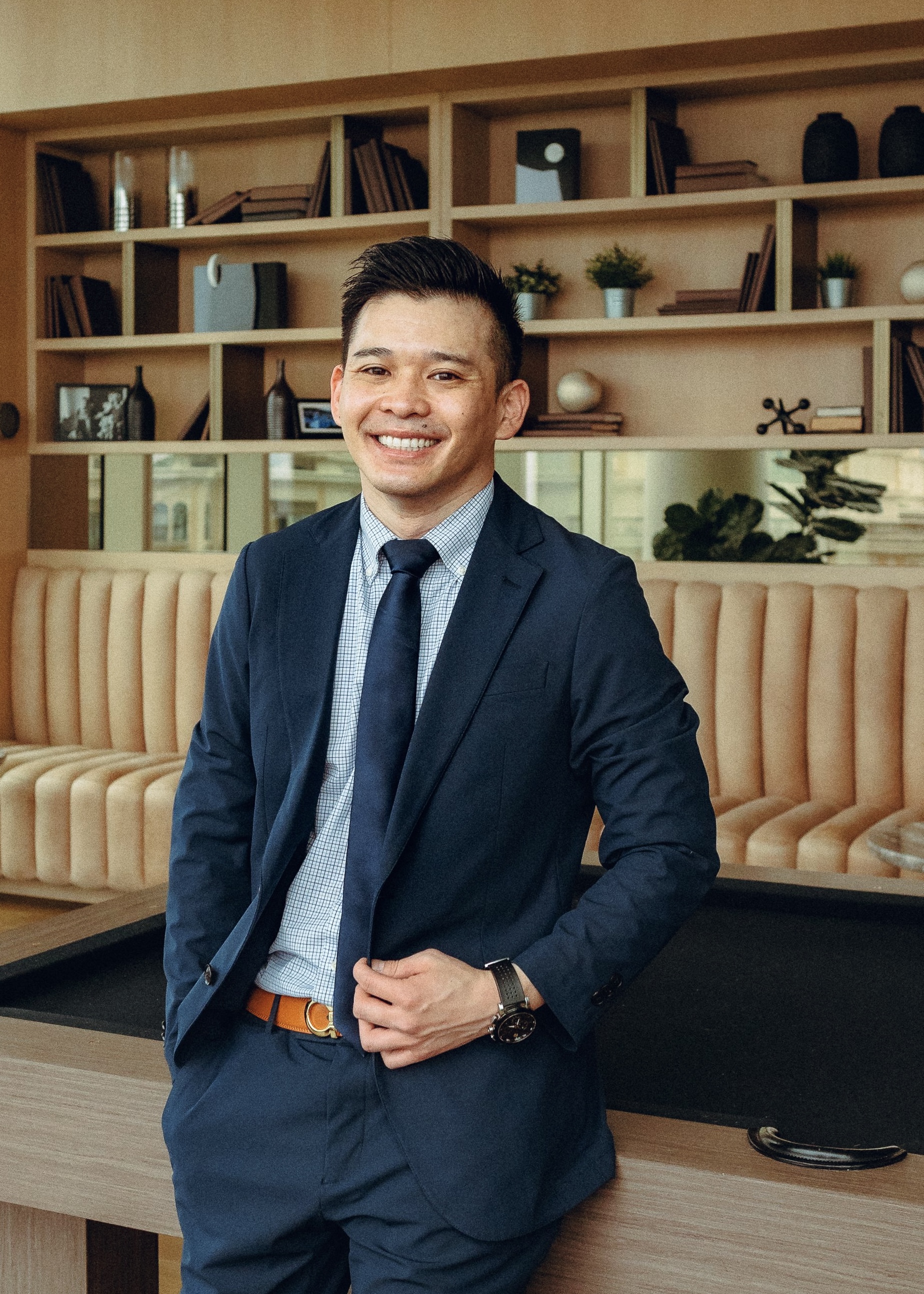 A photo of attorney Ron Ruangtragool, Esq. standing in front a of pool table, in front of a bookcase, and he is smiling.