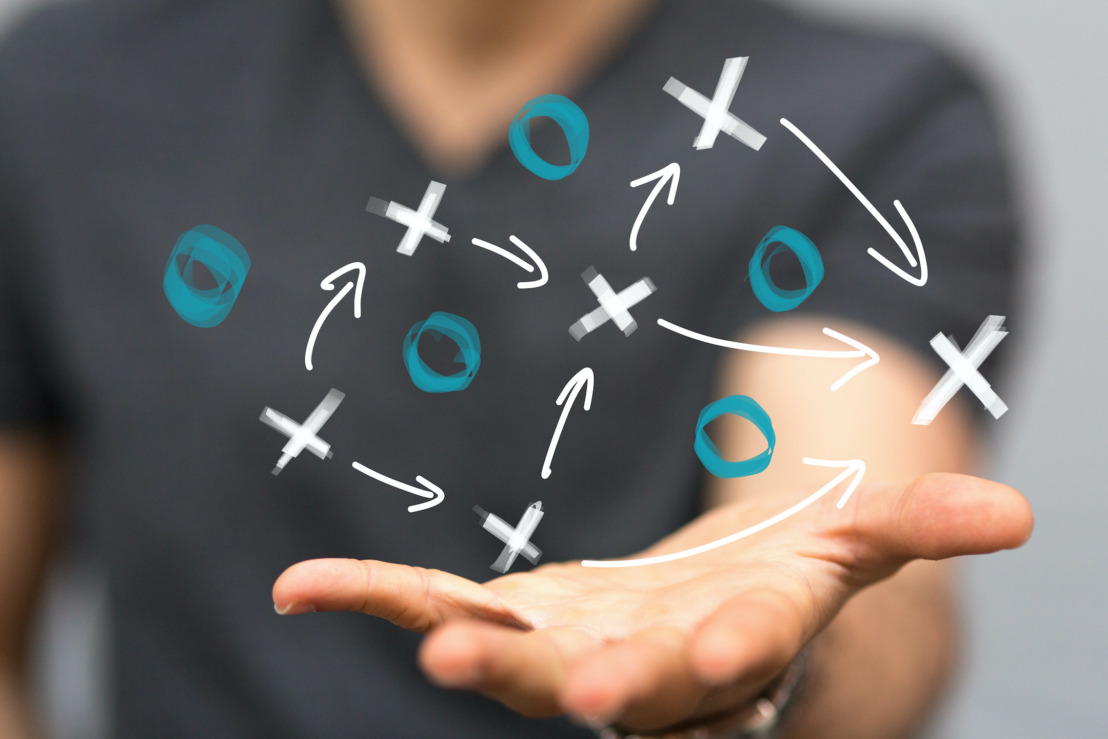 A photo of a hand extended toward the viewer with x's, o's, and arrows like a coach's playbook floating in mid-air.